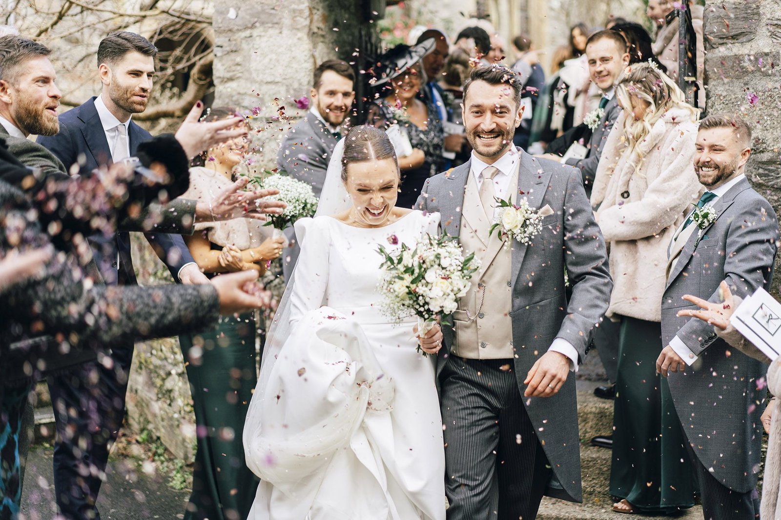 Bride and groom walk hand in hand through a shower of confetti in Plympton