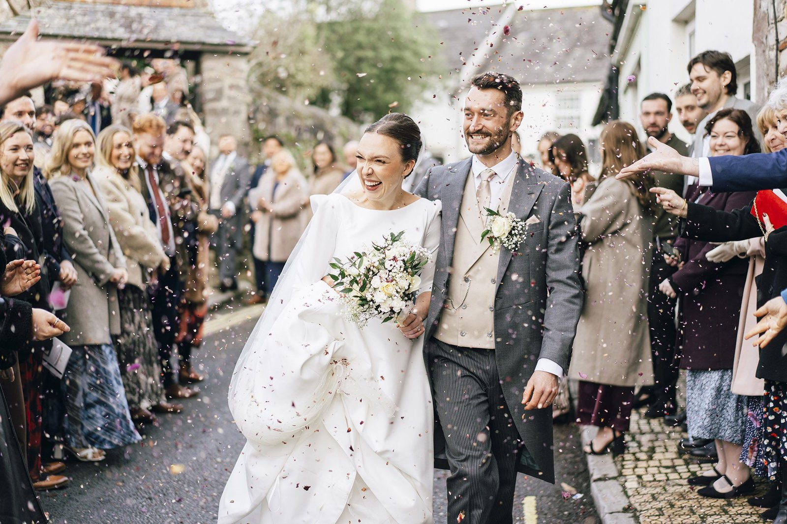 Bride and groom walk hand in hand through a shower of confetti outside St Elizabeth’s House, Plympton